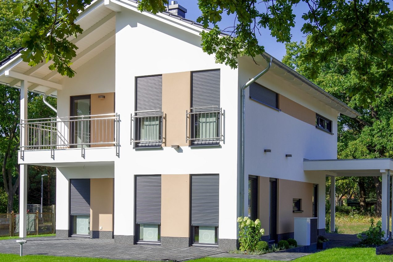 Immobilienfotografie Modernes zweistöckiges Wohnhaus mit Balkon und großen Fenstern, umgeben von Bäumen.